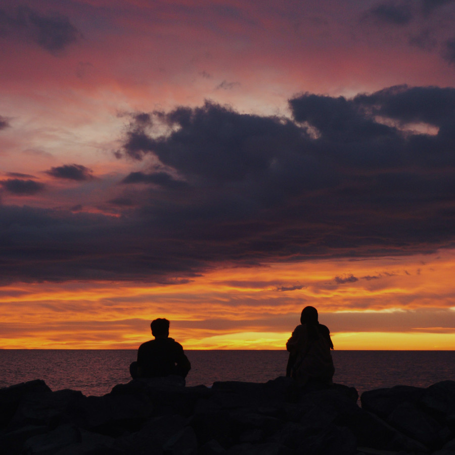 Two people sitting together on a rock, looking out over the water