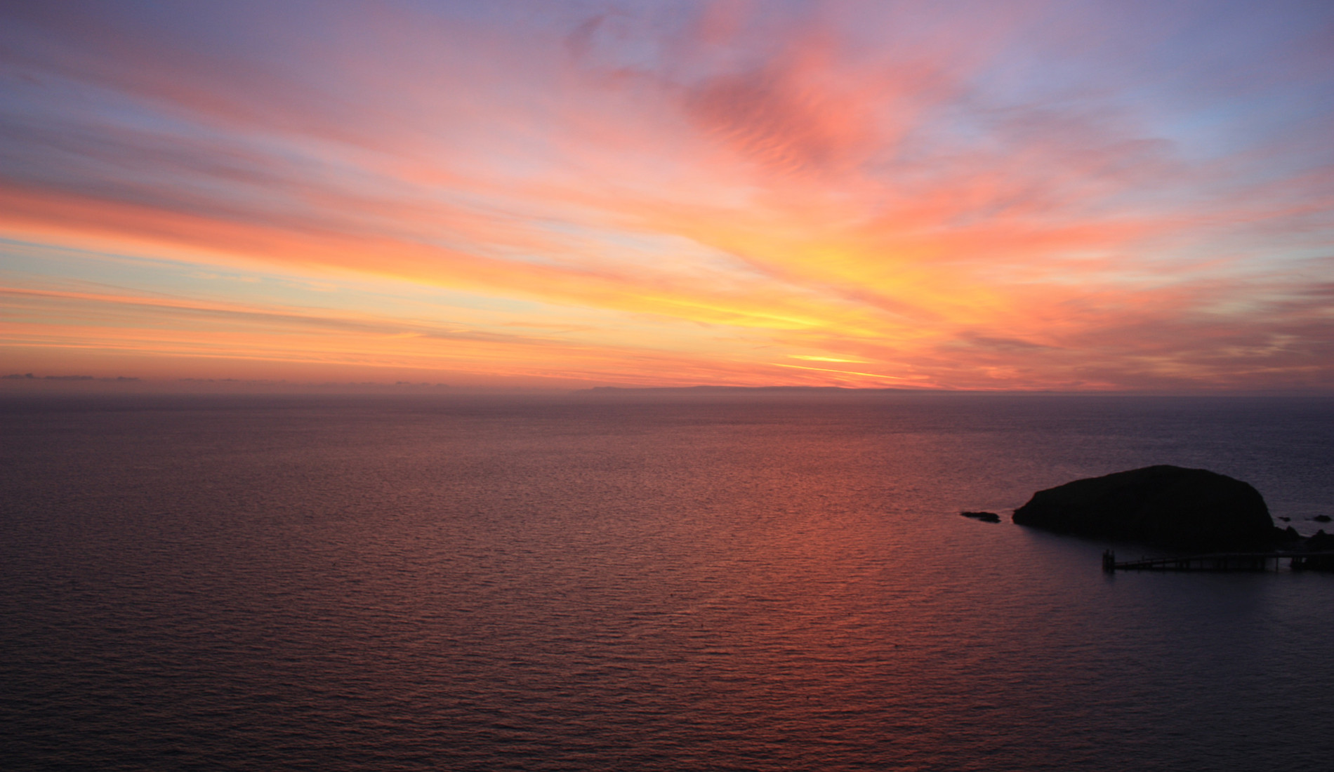 Still ocean water at sunrise, a small island silhouetted on the horizon